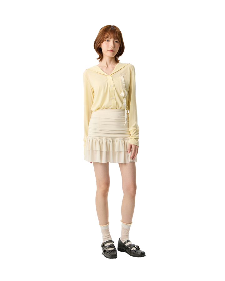 Woman wearing a light yellow outfit with a skirt on a white background