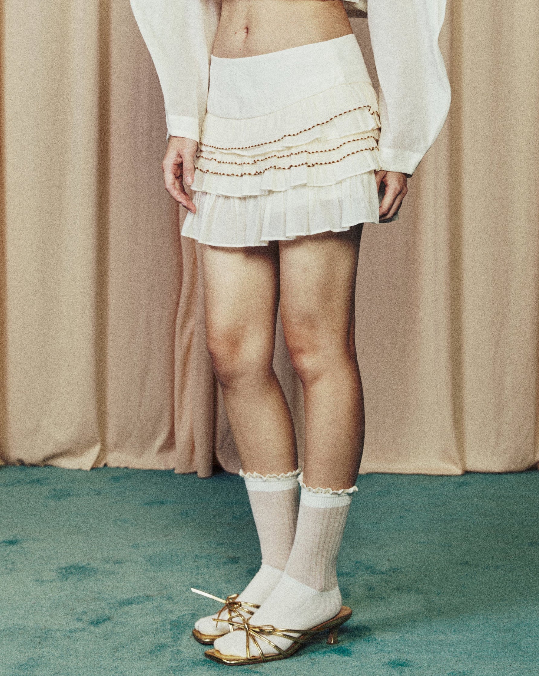 Person wearing a white outfit with a beige curtain background