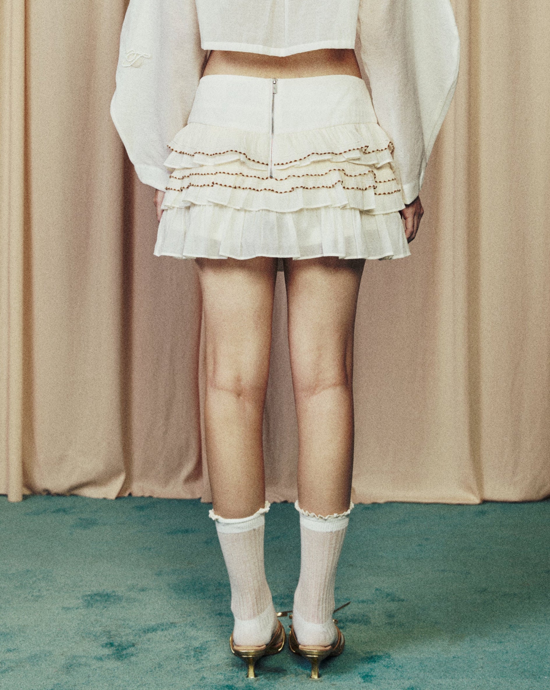 Person wearing a white outfit standing in front of beige curtains