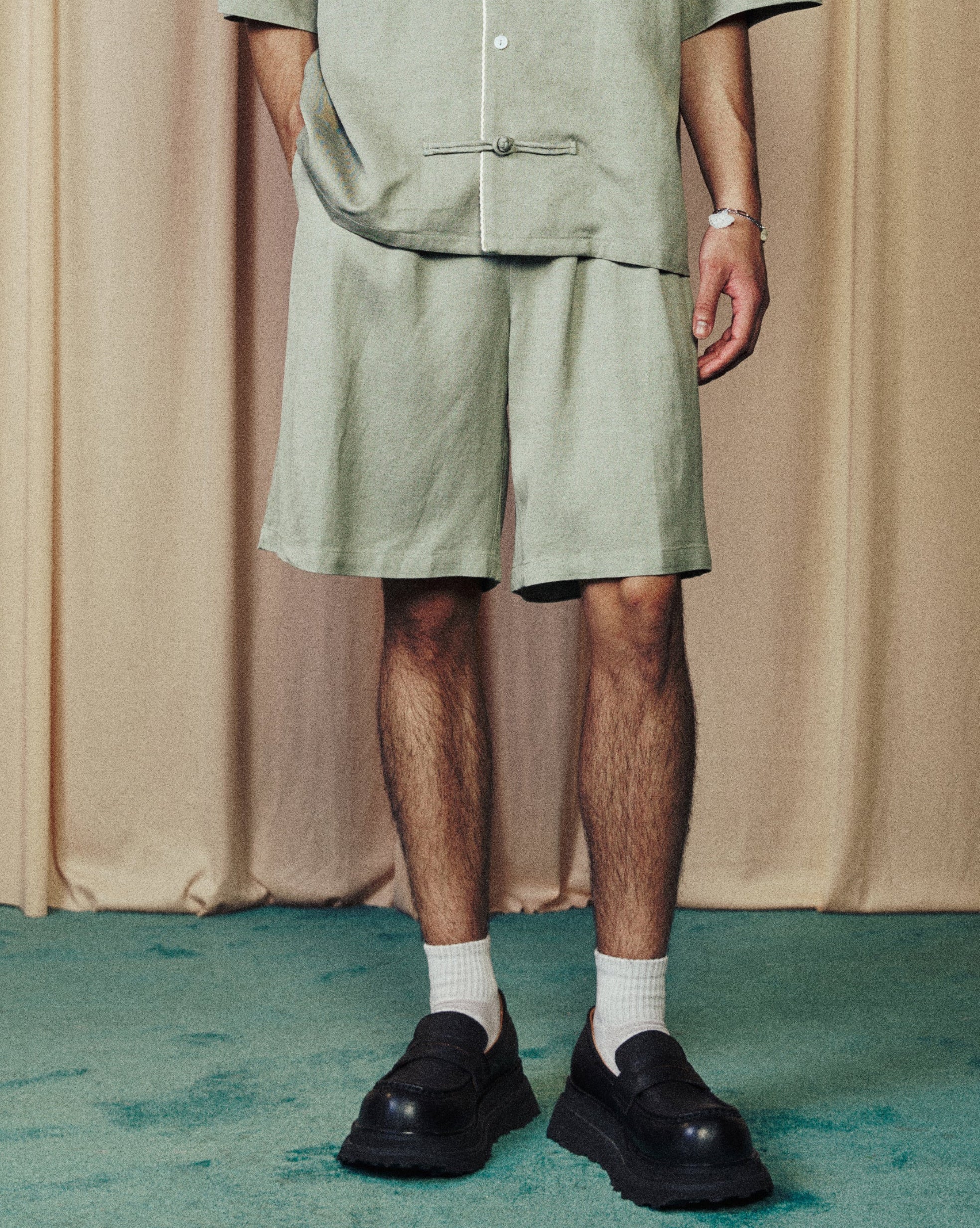 Person wearing a green outfit standing in front of beige curtains.