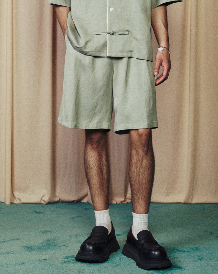 Person wearing a green outfit standing in front of beige curtains.