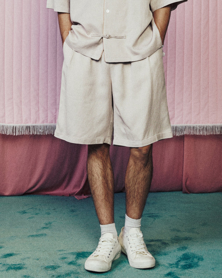Person wearing a beige outfit standing in front of pink curtains with a heart shape.