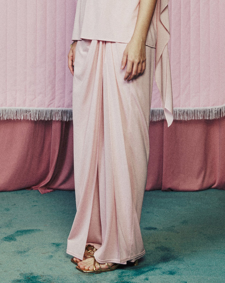 Woman in a light pink outfit standing in front of a heart-shaped curtain