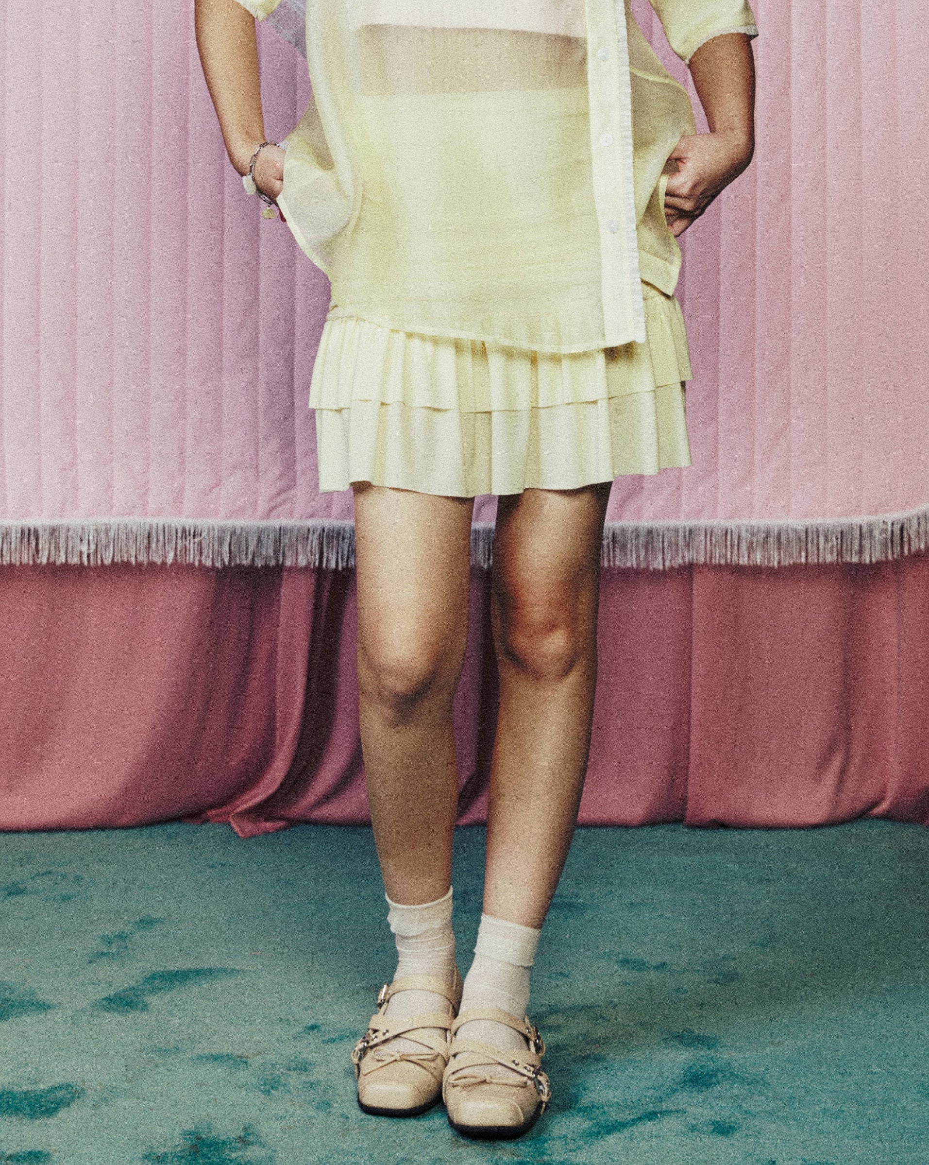 Person wearing a light-colored outfit standing in front of pink curtains with a heart shape.